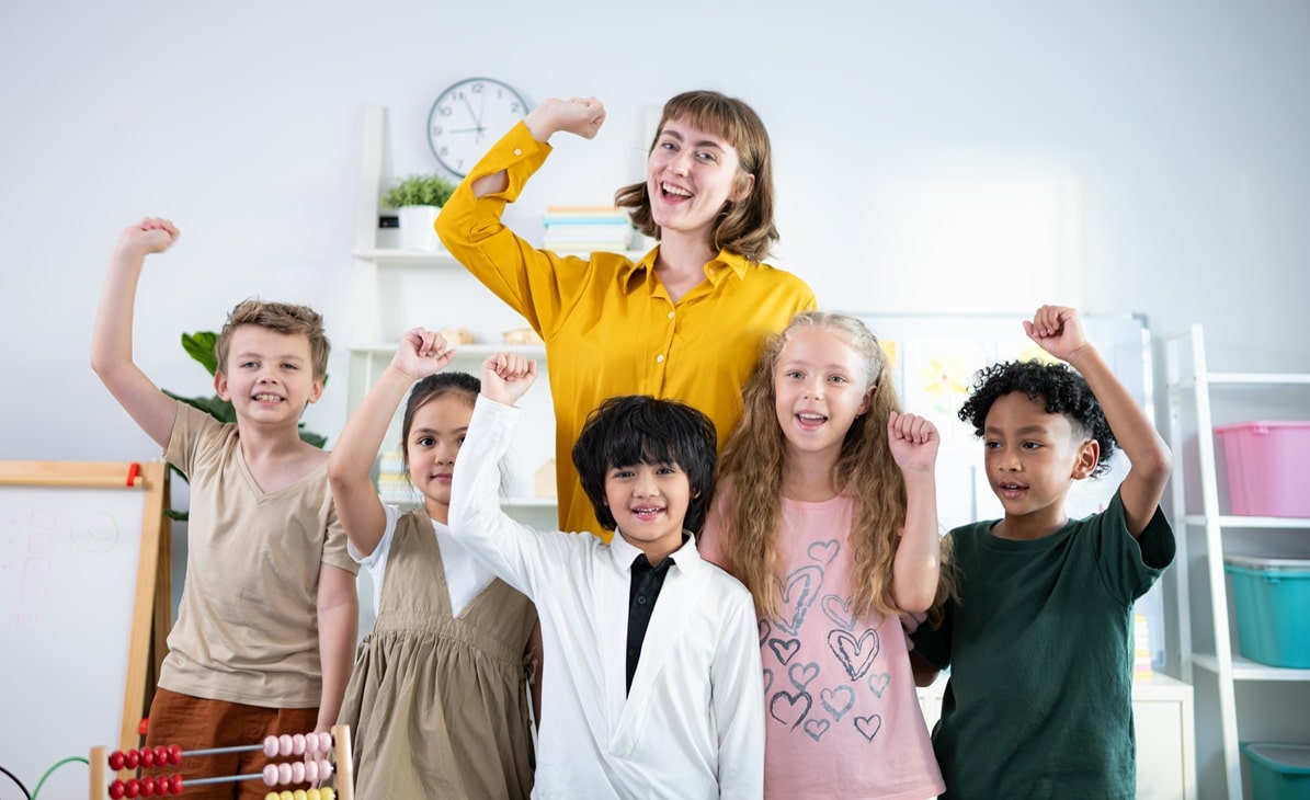 A group of children and their teacher doing a mustle sign to show confidence within the class room.