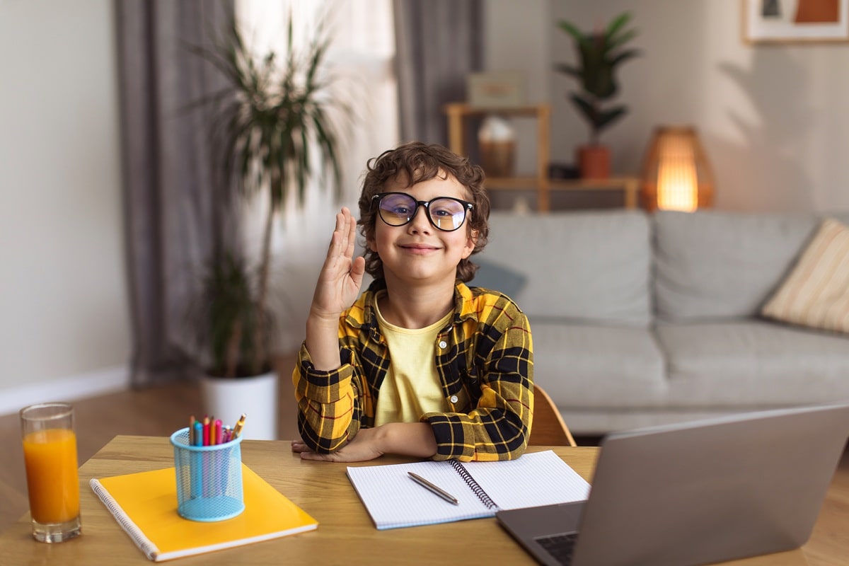 A young boy with his hand raised in an online tutor session for ATTC Education.