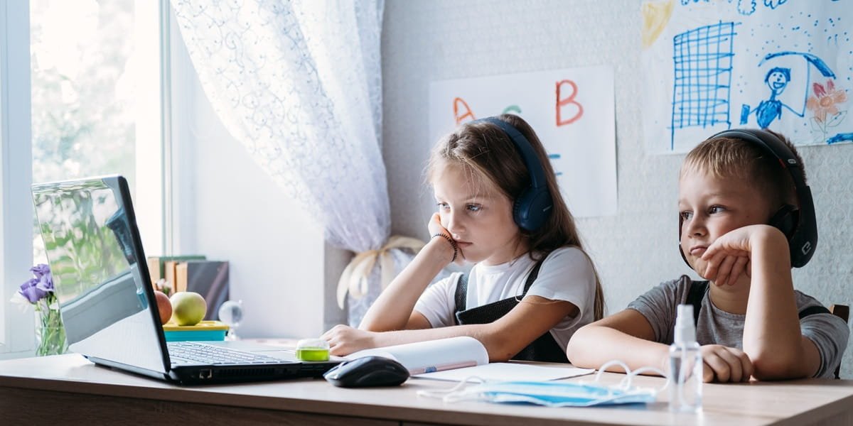 Two young kids having an online lesson at home.