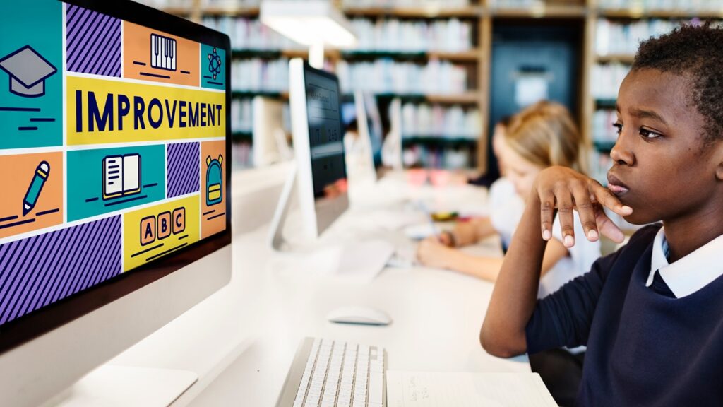 A computer with the words imprvement on the screen with a boy looking at it.
