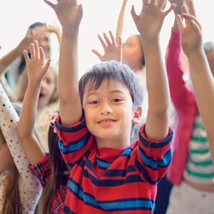 A young boy in a class room with his hands in the air.