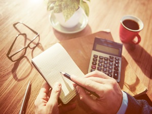 A business man using a note pad with a calculator and coffee in the background.