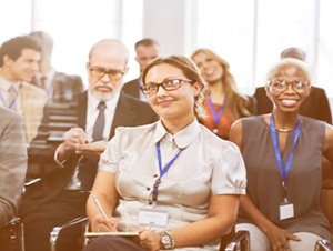 A group of adults sat watching a presentation or conference.