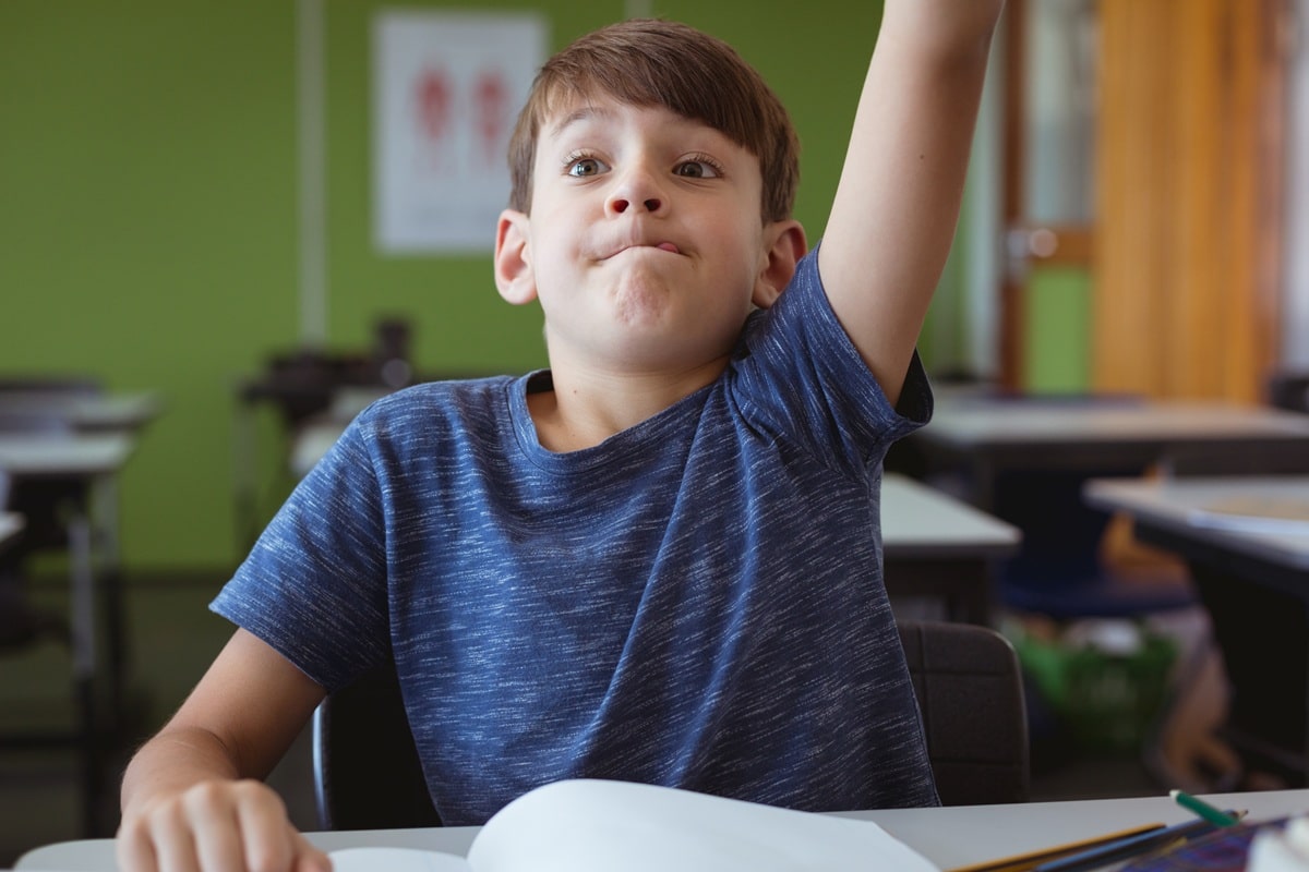 A young boy with hand-up in classroom, showing confidence improving.
