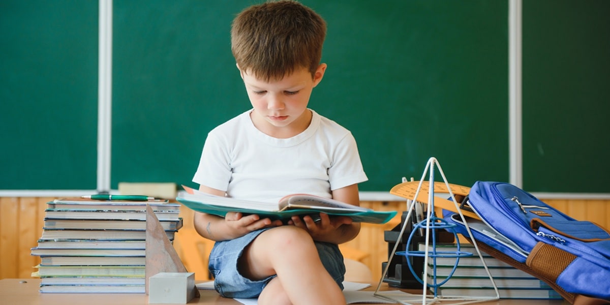 A little boy reading next to a stack of books.