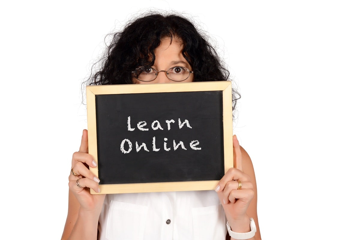 A lady holding a wooden sign with the words Learn online in chalk on them.