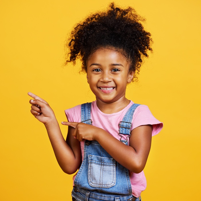 Studio portrait mixed race girl pointing sideways towards copyspace isolated against a yellow backg.
