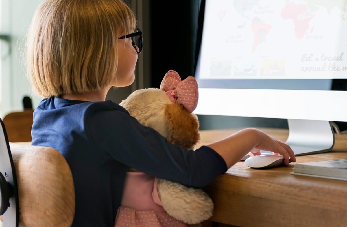 66617027_l A young girl doing an online lesson on her computer with her teddy bear in her hands.