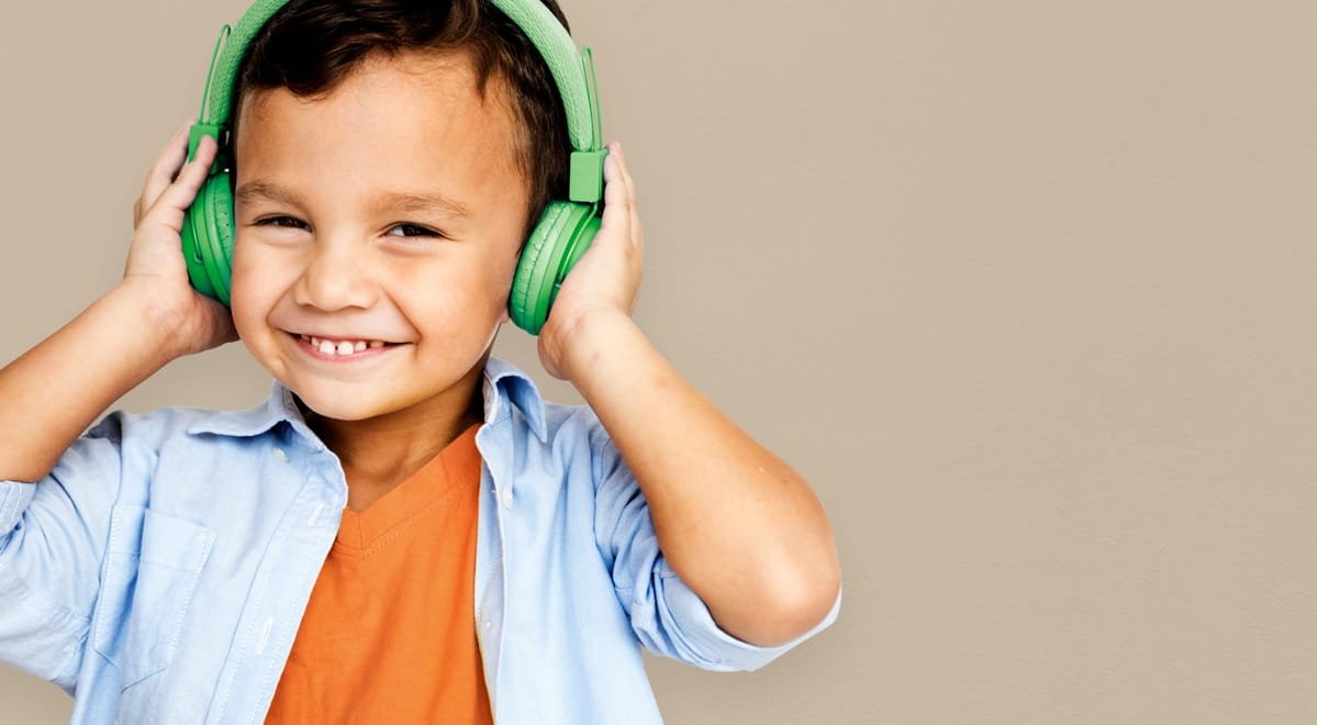 A little boy wearing green headphones with a smile on his face.