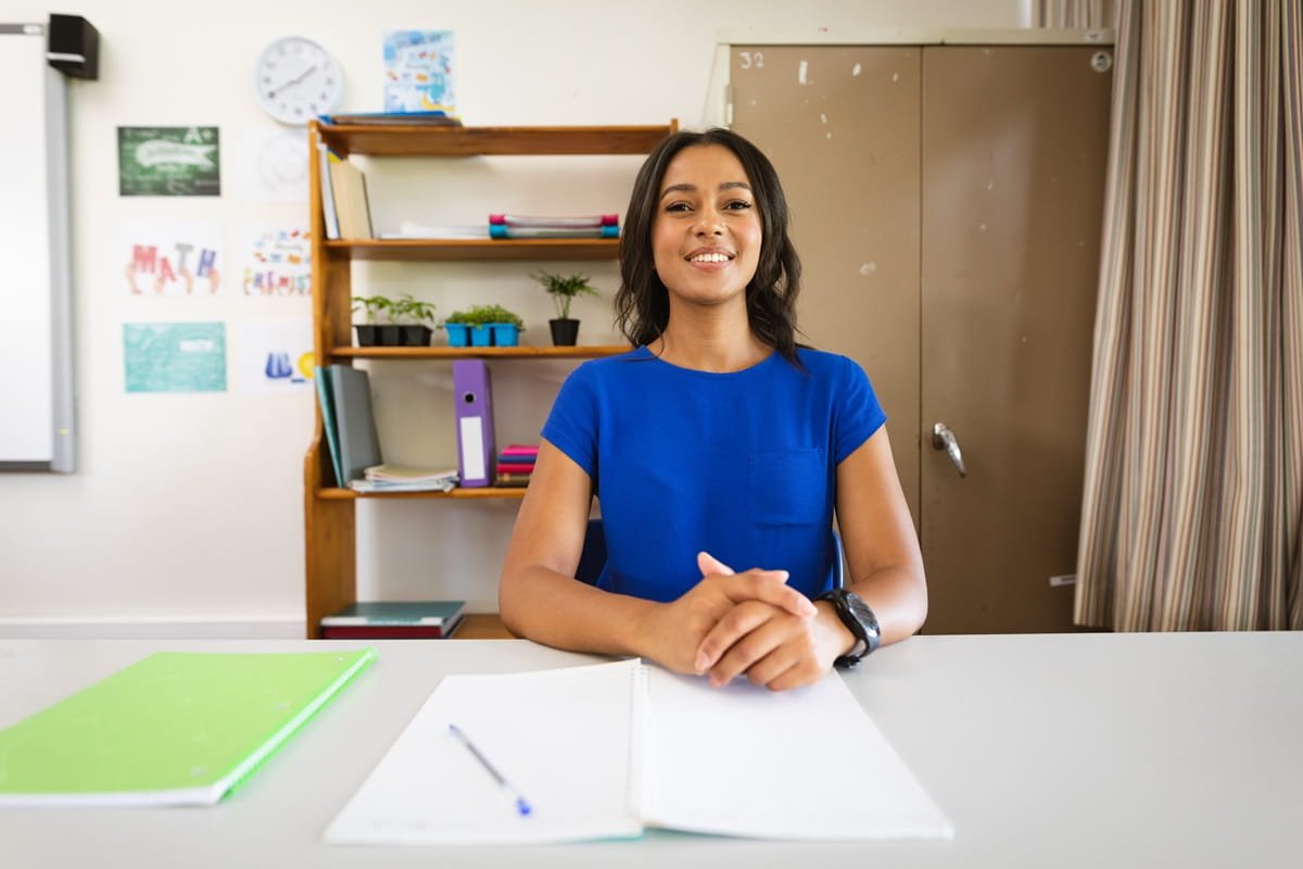 A young teacher smiling in her office with papers in front of her.