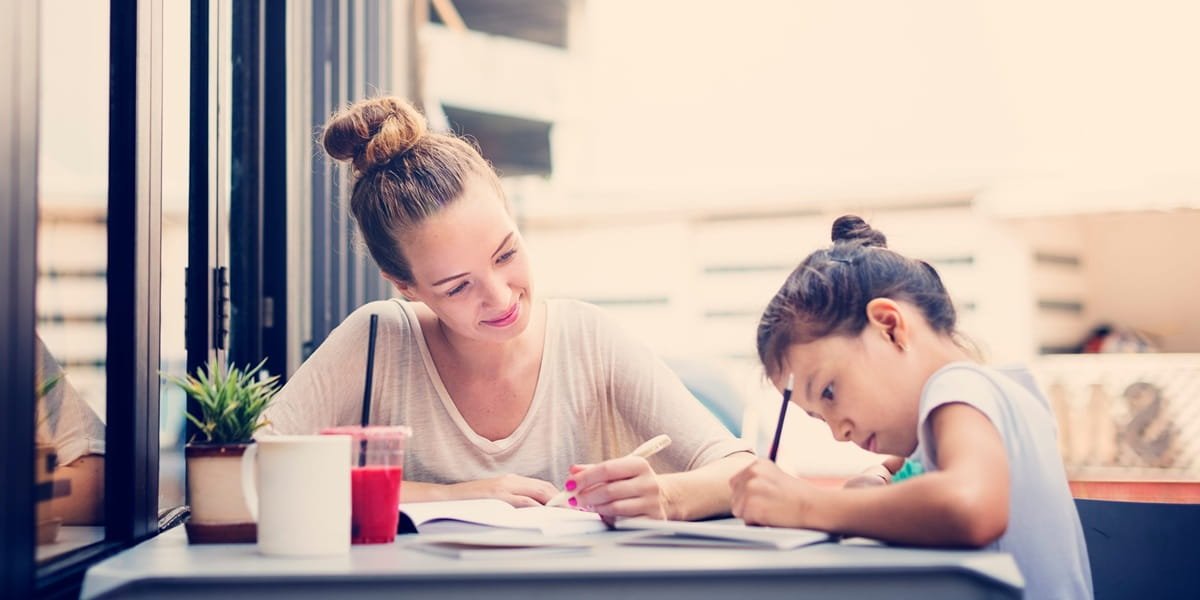 A young girl doing writing with her mum in a light area of the garden.